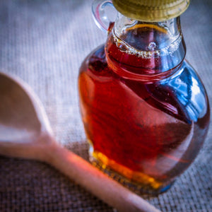 A glass jar full of delicious maple syrup next to a wooden spoon